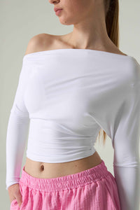 Person wearing a white off-shoulder top and pink pants against a plain background.