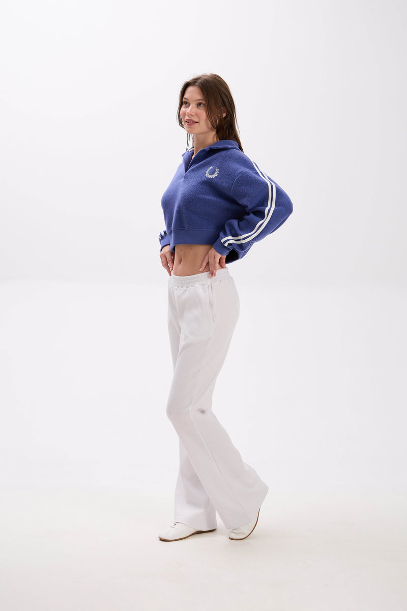 Person wearing a blue tracksuit with white pants on a white background.