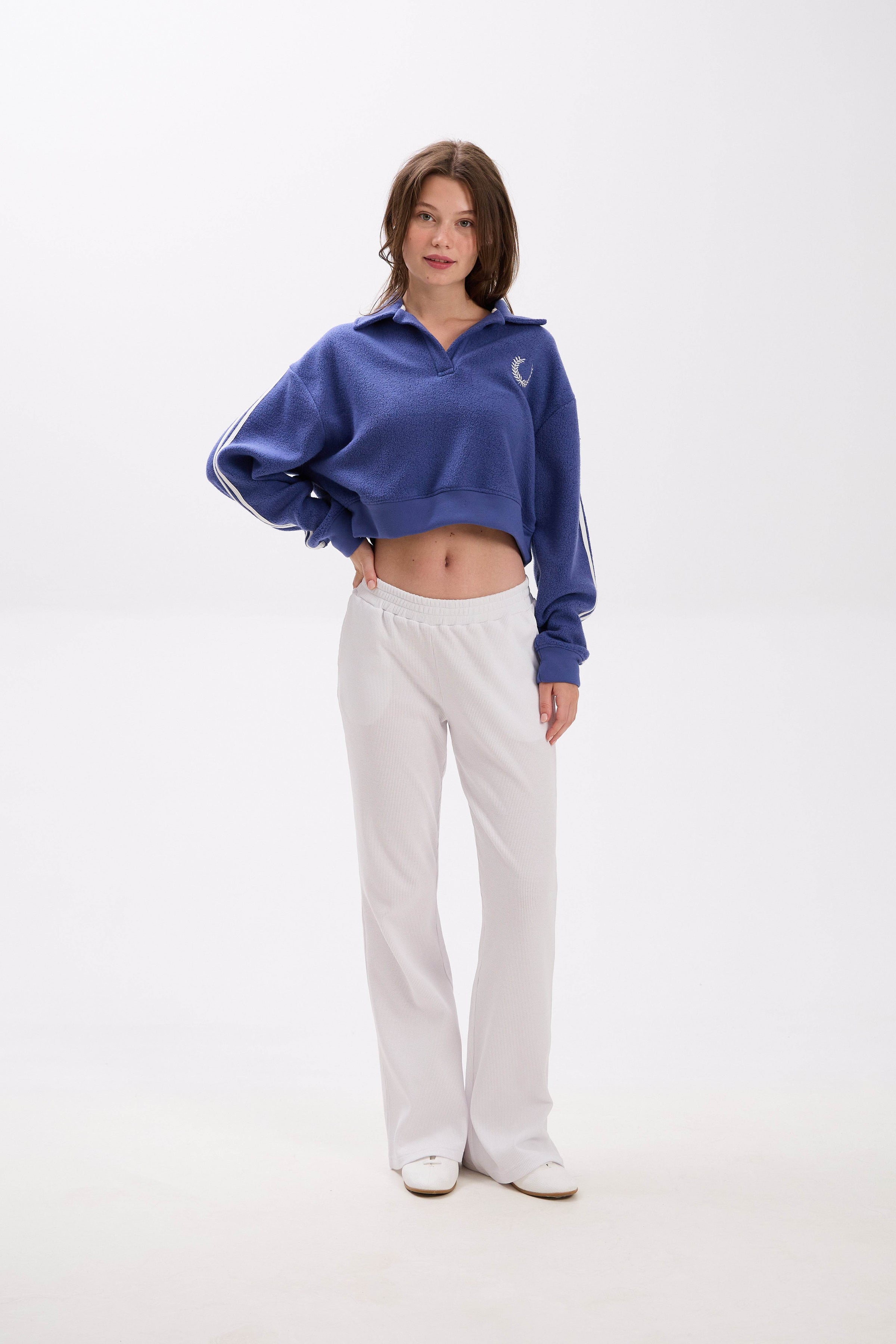 Person wearing a blue cropped jacket and white pants on a white background.