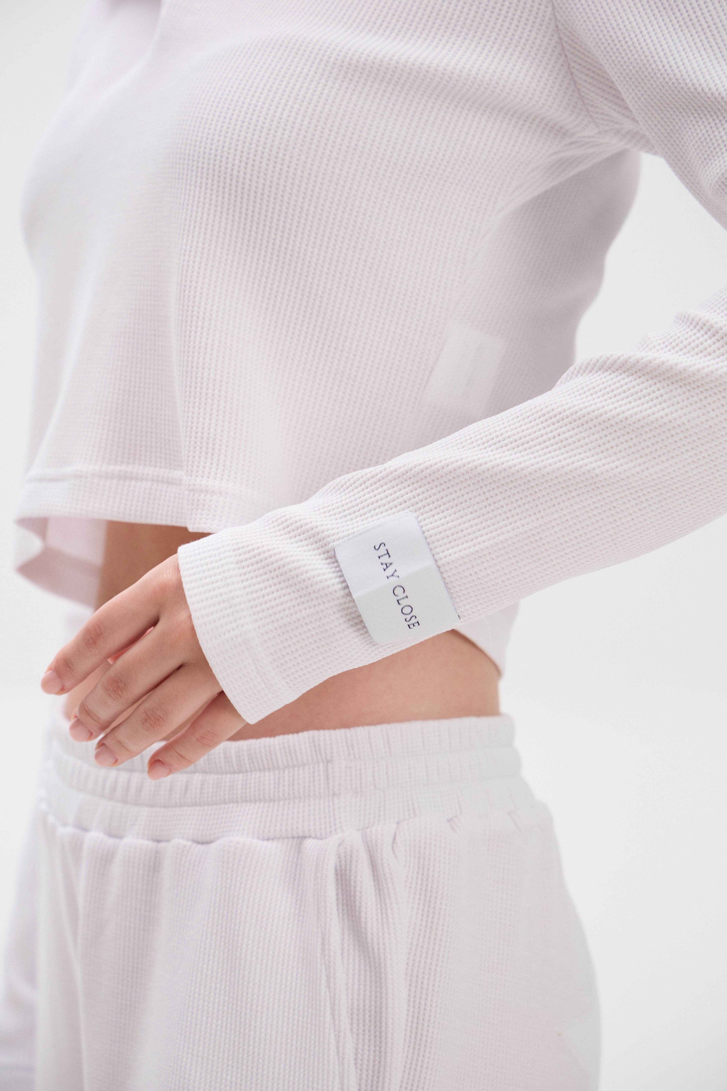 Person wearing a white long-sleeve top and pants with a visible brand label "STAY CLOSE".