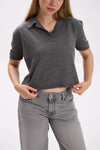 Person wearing a gray cropped polo shirt and gray jeans on a white background