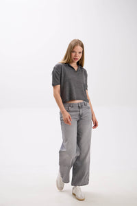 Woman wearing a dark gray polo shirt and light gray jeans on a white background