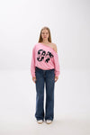 Model wearing a pink off-shoulder sweatshirt with bold “Stay Close” print, styled with blue jeans and white sneakers.