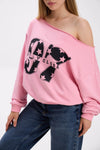 Close-up of pink off-shoulder sweatshirt with bold black “Stay Close 97” print, styled with blue jeans.