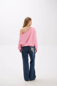 Back view of model in a pink off-shoulder sweatshirt paired with blue jeans featuring a large star detail on the leg.