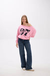 Model in a pink off-shoulder sweatshirt with bold black “Stay Close 97” print, paired with blue jeans and sneakers.