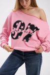 Close-up of pink off-shoulder sweatshirt with large black “Stay Close 97” print, styled with blue jeans.