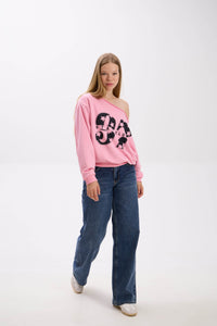 Model walking in a pink off-shoulder sweatshirt with bold black “Stay Close 97” print, styled with blue jeans and sneakers.