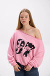 Model wearing a pink off-shoulder sweatshirt with bold black “Stay Close 97” print, paired with blue jeans.