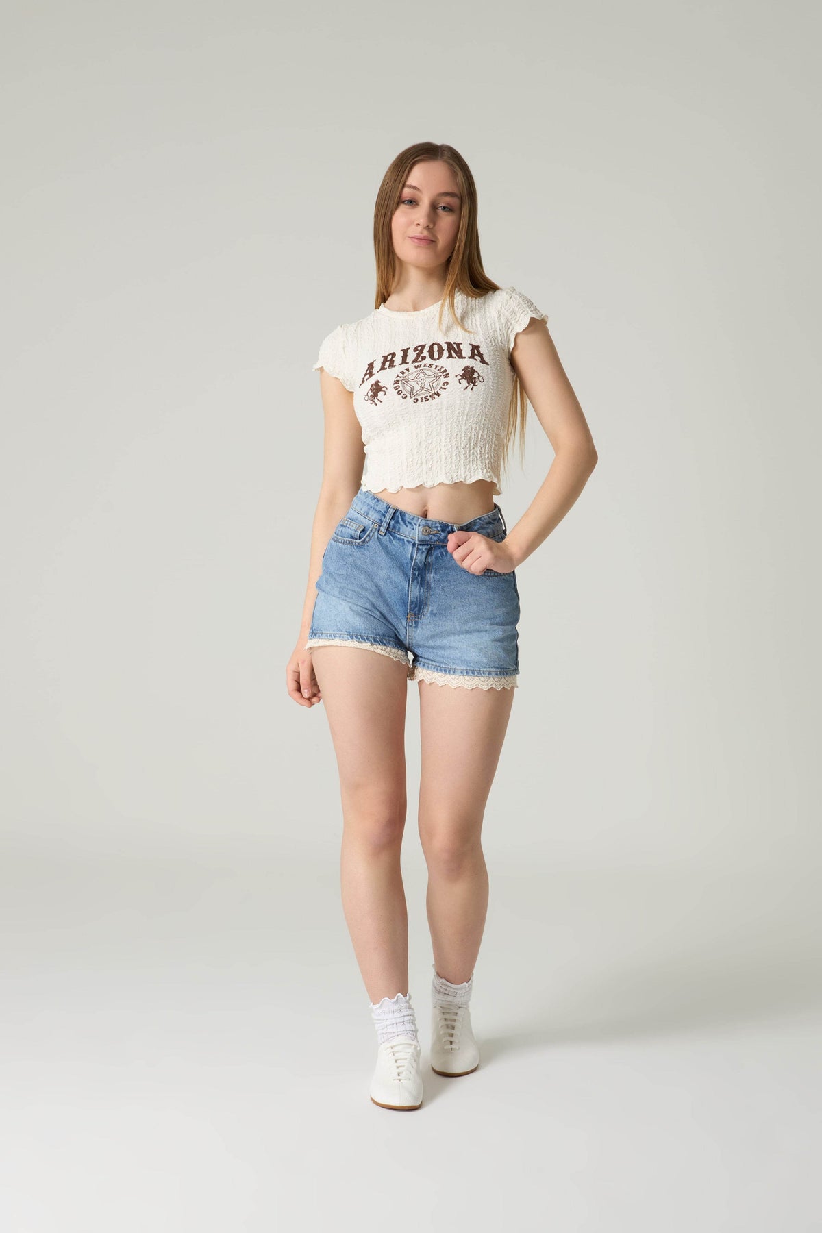 Person wearing a white t-shirt with 'Arizona' print and denim shorts on a plain background.