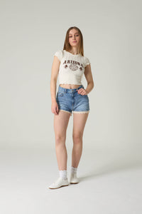 Woman wearing a white crop top with text and denim shorts on a plain background.
