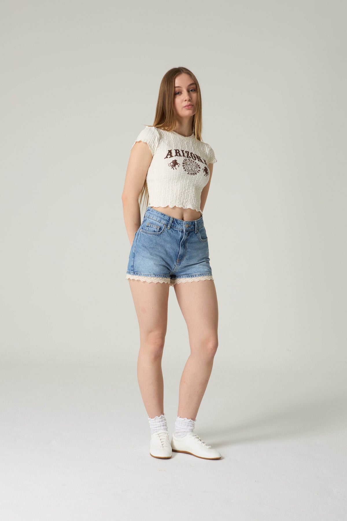 Woman wearing a white t-shirt with text and blue denim shorts on a plain background.