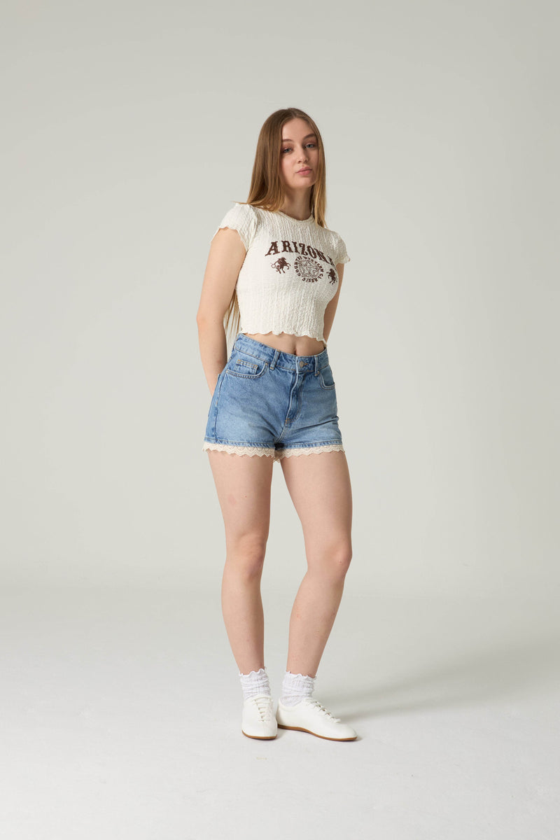 Woman wearing a white t-shirt with text and blue denim shorts on a plain background.