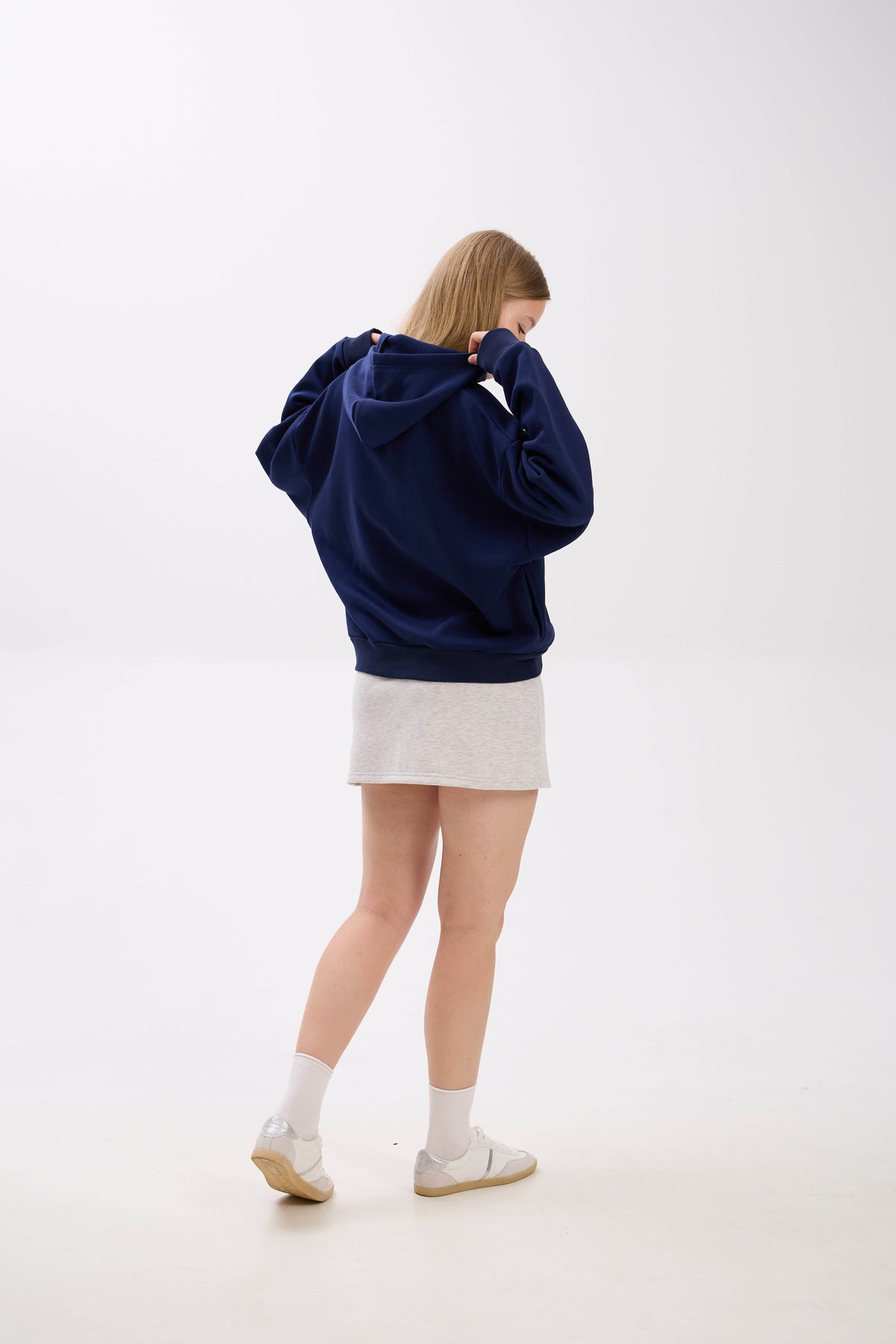 Person wearing a navy blue hoodie and white skirt on a white background