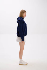 Person wearing a navy blue hoodie and white skirt on a white background