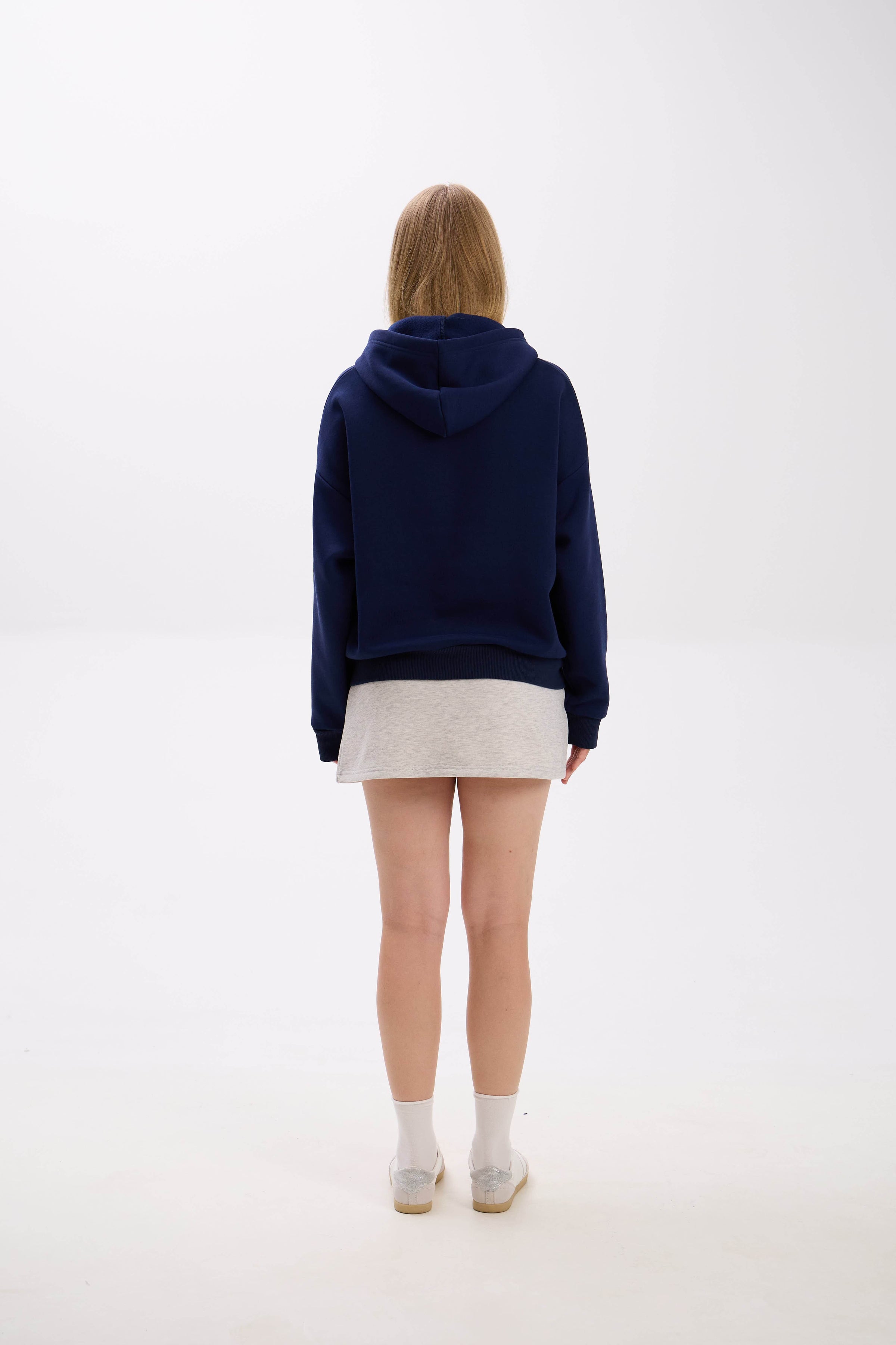 Person wearing a navy blue hoodie and white skirt on a white background