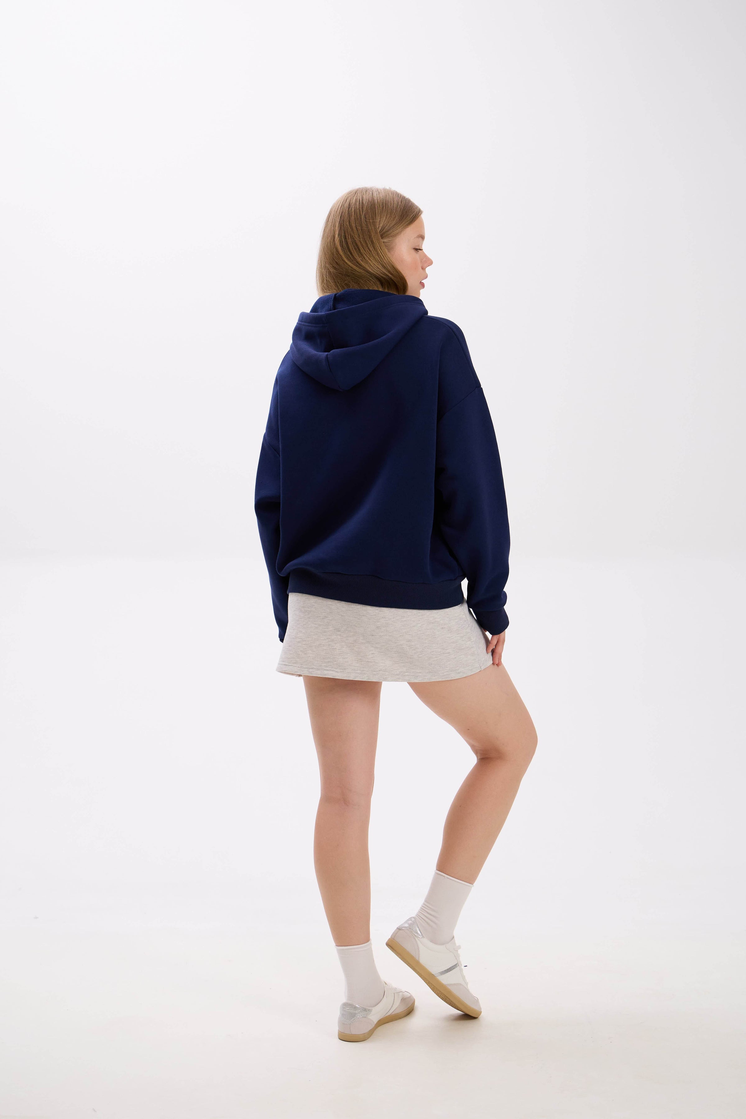Person wearing a navy blue hoodie and beige skirt on a white background