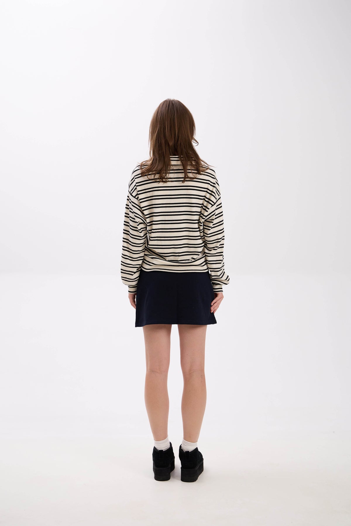 Person wearing a striped sweater and black skirt on a white background