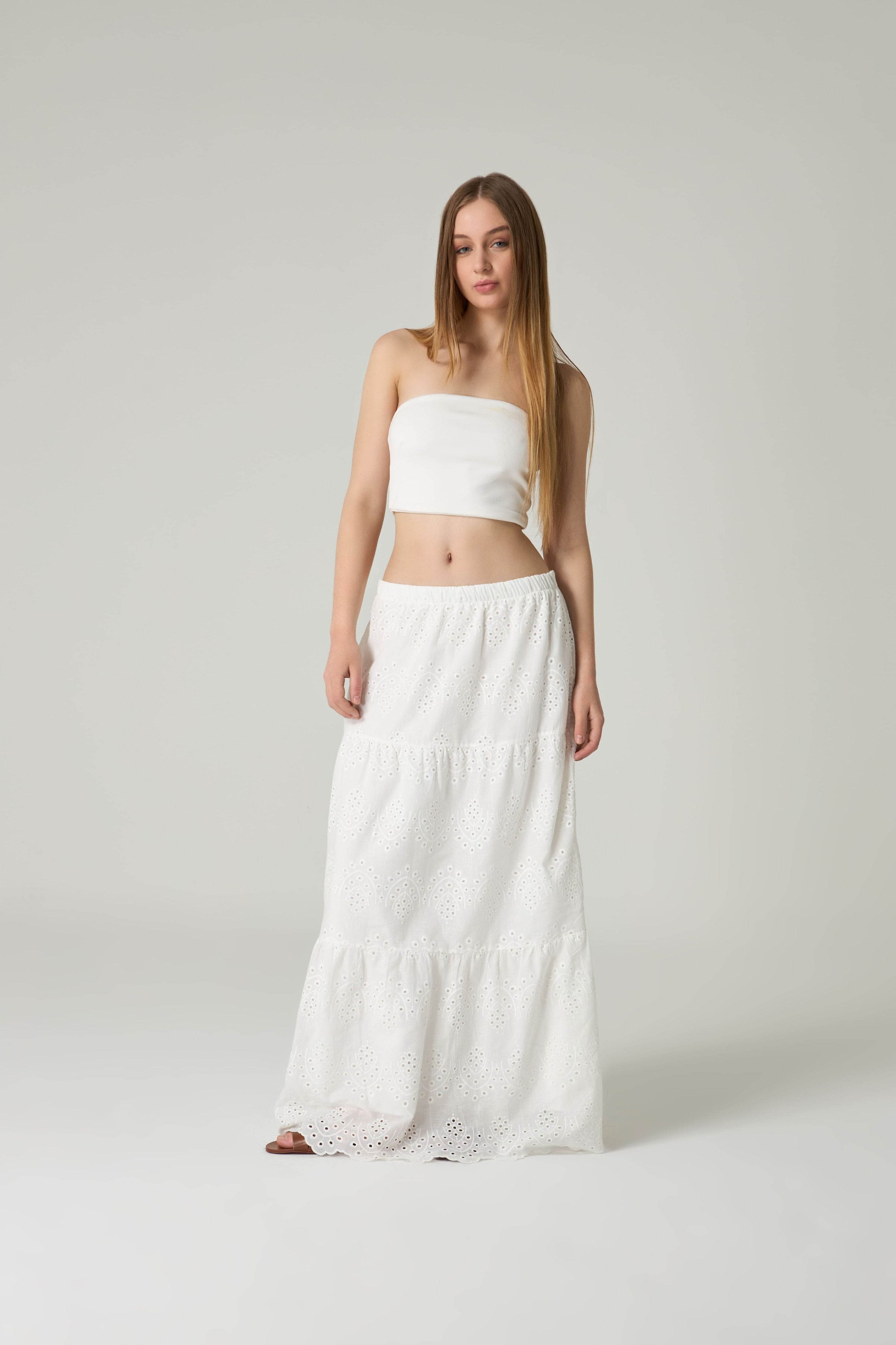 Woman wearing a white strapless top and long white skirt on a plain background.