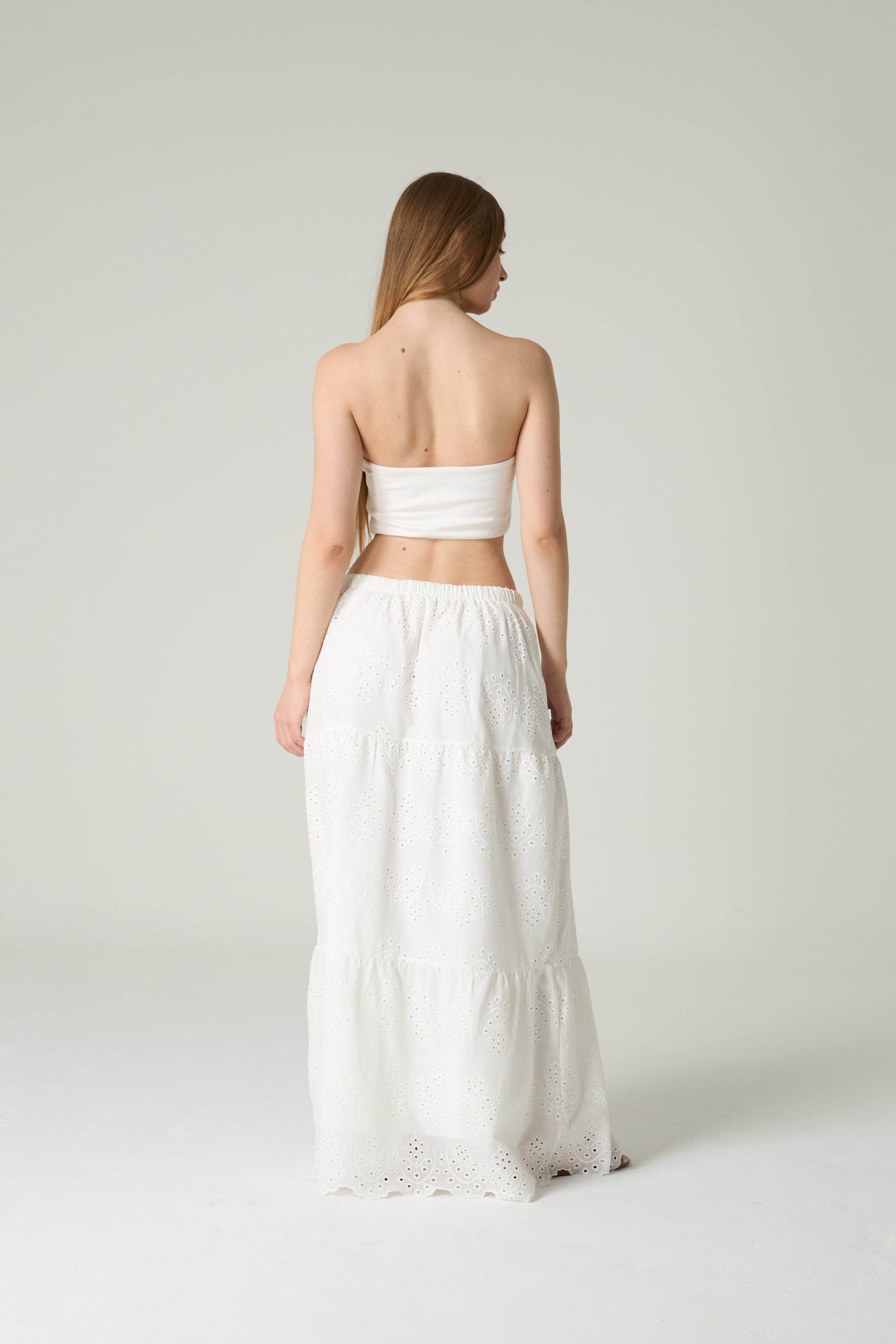 Woman wearing a white strapless top and skirt set on a plain background.