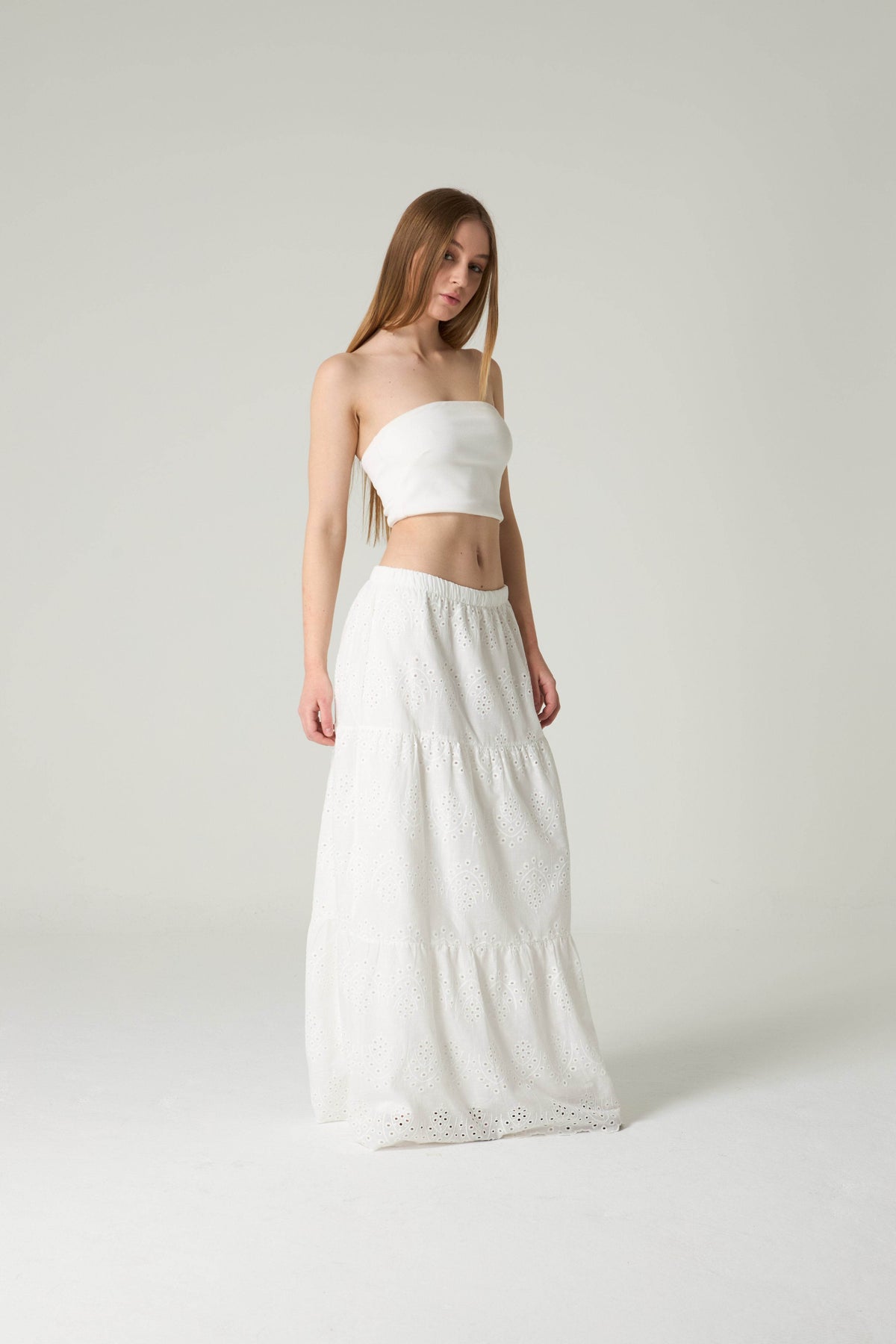 Woman wearing a white strapless top and long skirt on a plain background.