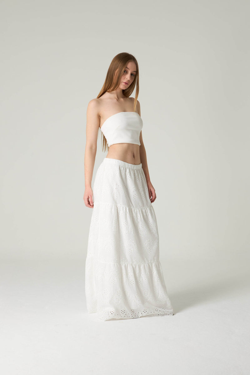 Woman wearing a white strapless top and long skirt on a plain background.