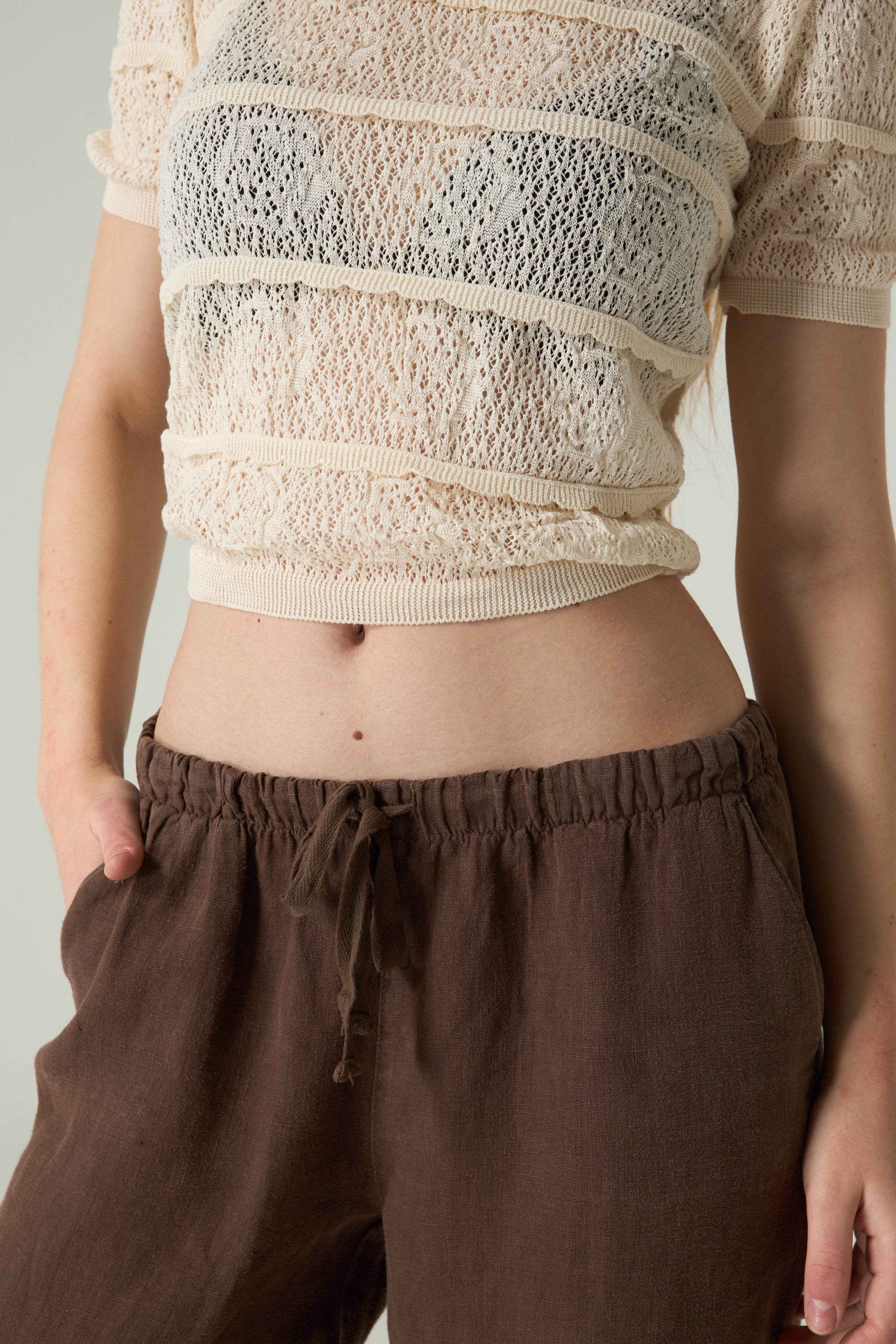 Person wearing a beige textured top and brown pants against a neutral background.