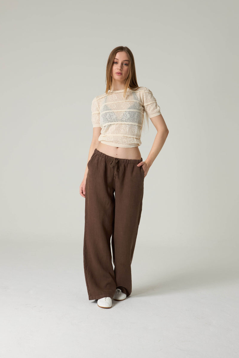 Woman wearing a beige top and brown pants on a white background.