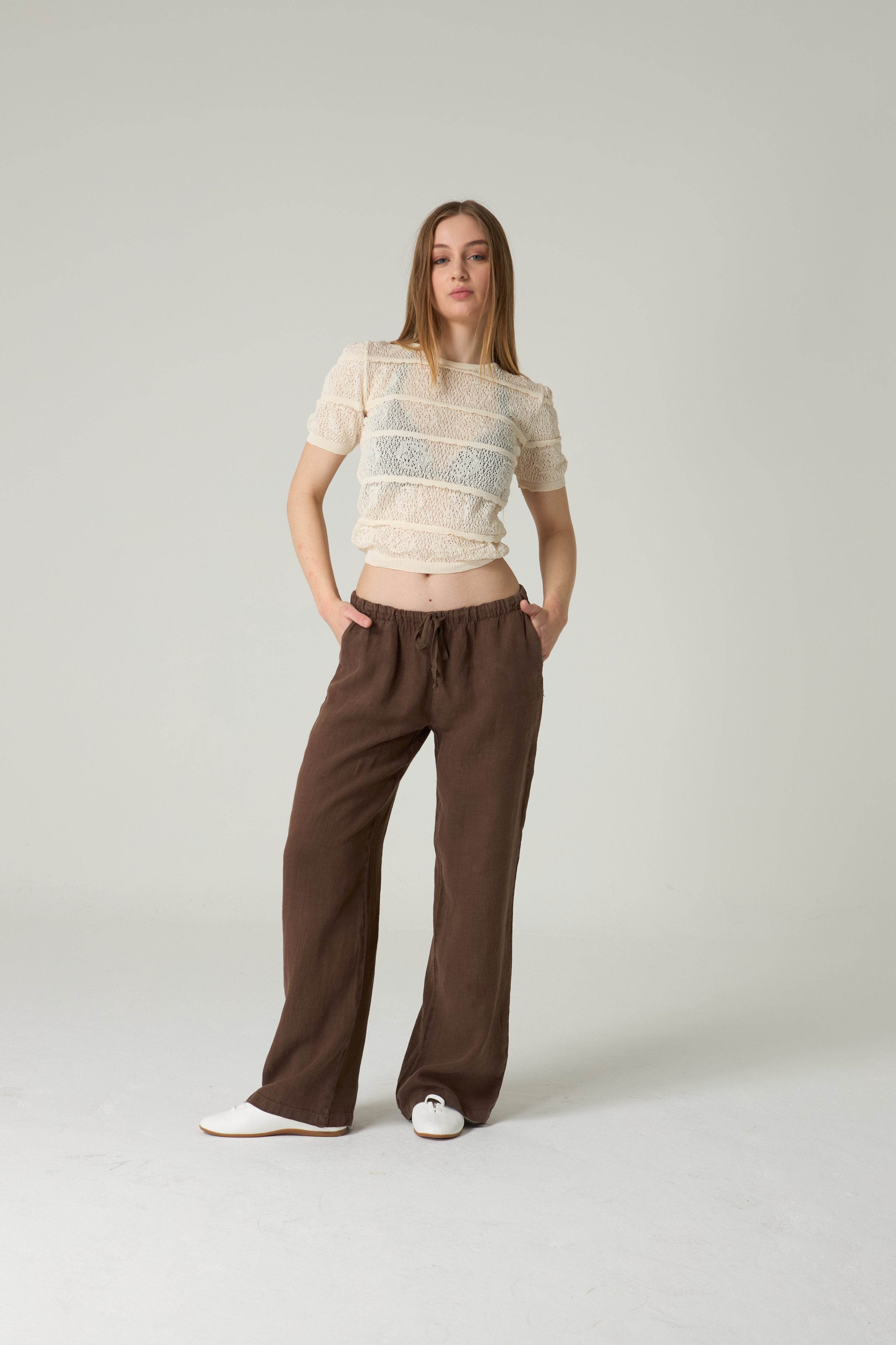 Woman wearing a beige top and brown pants on a plain background.