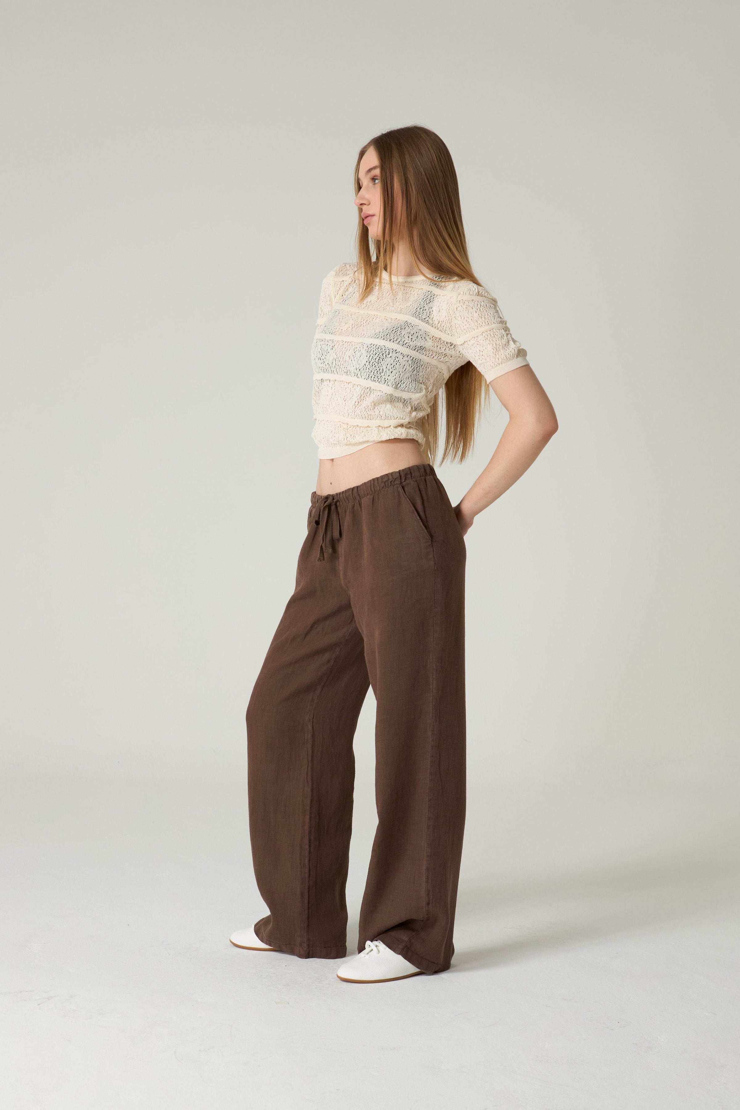 Woman wearing a beige top and brown pants on a white background.