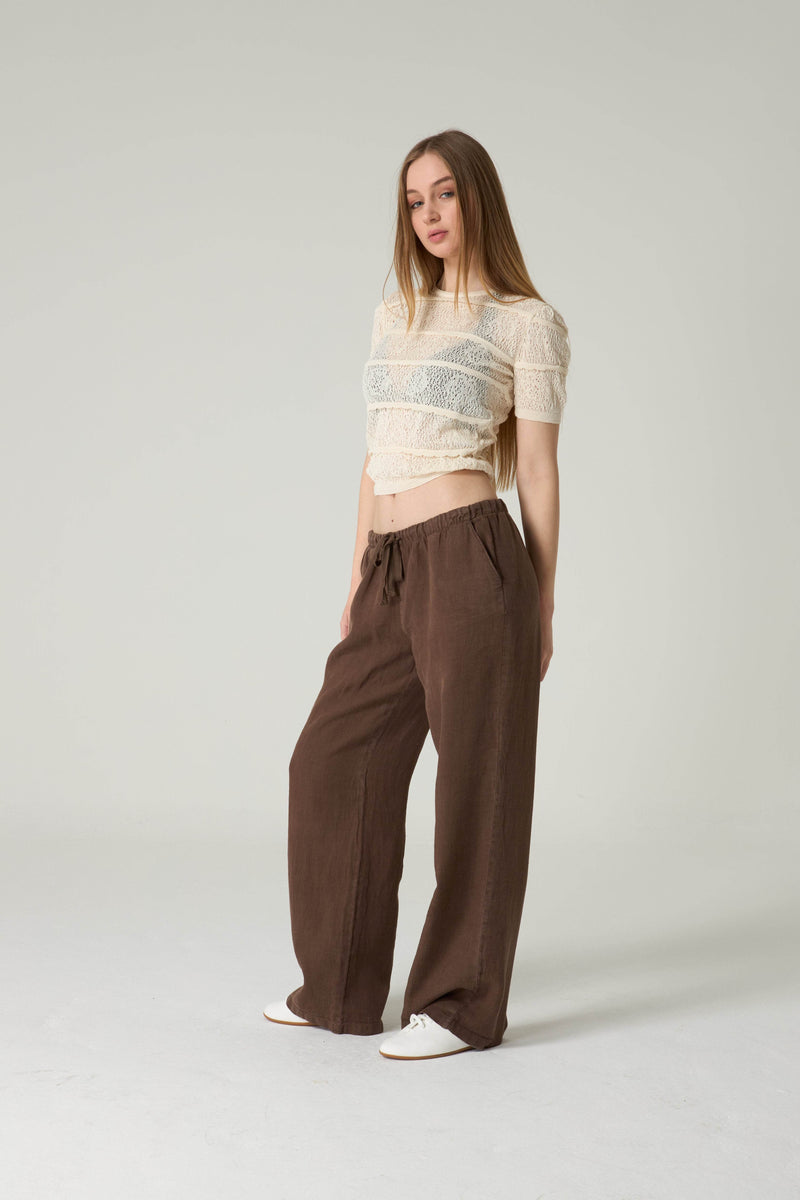 Woman wearing a beige top and brown pants on a plain background.