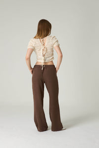 Person wearing a beige lace-up top and brown pants on a white background.