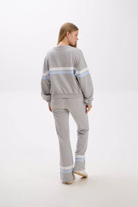 Woman wearing a gray sweater and pants with light blue stripes on a white background.