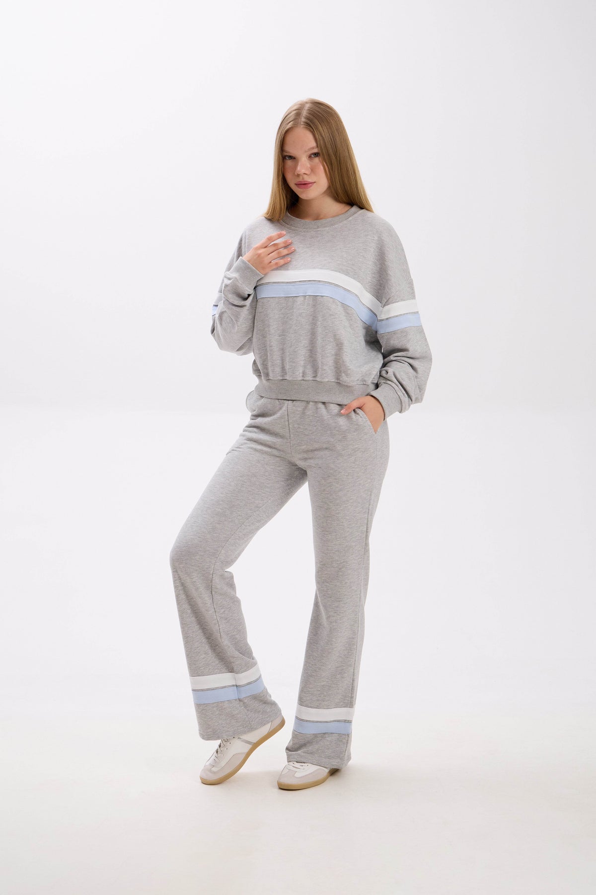 Woman wearing a gray tracksuit with light blue stripes on a white background.
