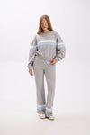 Woman wearing a gray sweater and pants with light blue stripes on a white background.