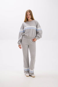 Woman wearing a gray sweater and pants with light blue stripes on a white background.