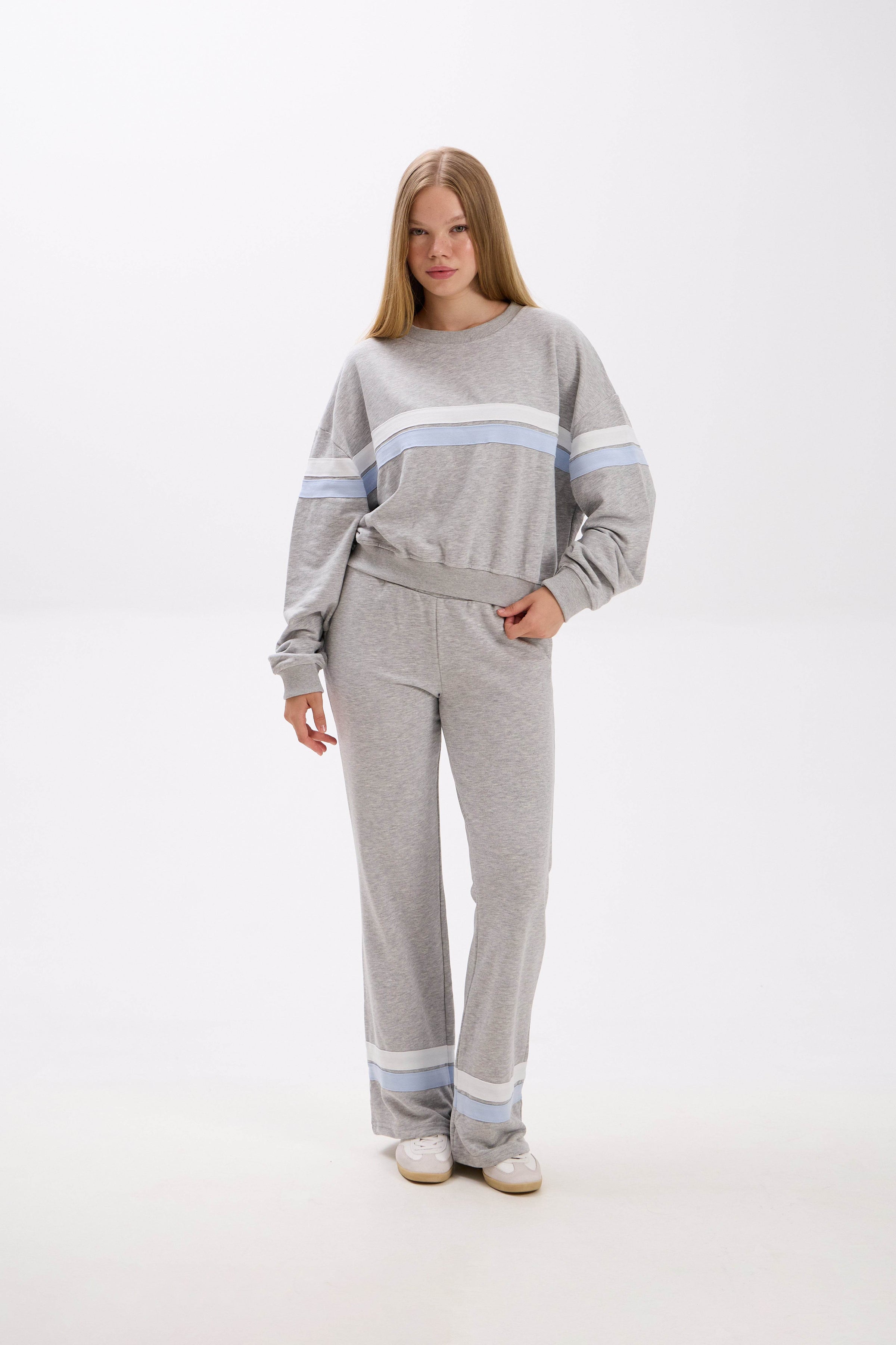 Woman wearing a gray sweater and pants with light blue stripes on a white background.