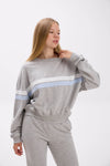 Woman wearing a gray sweatshirt with a blue stripe on a white background.