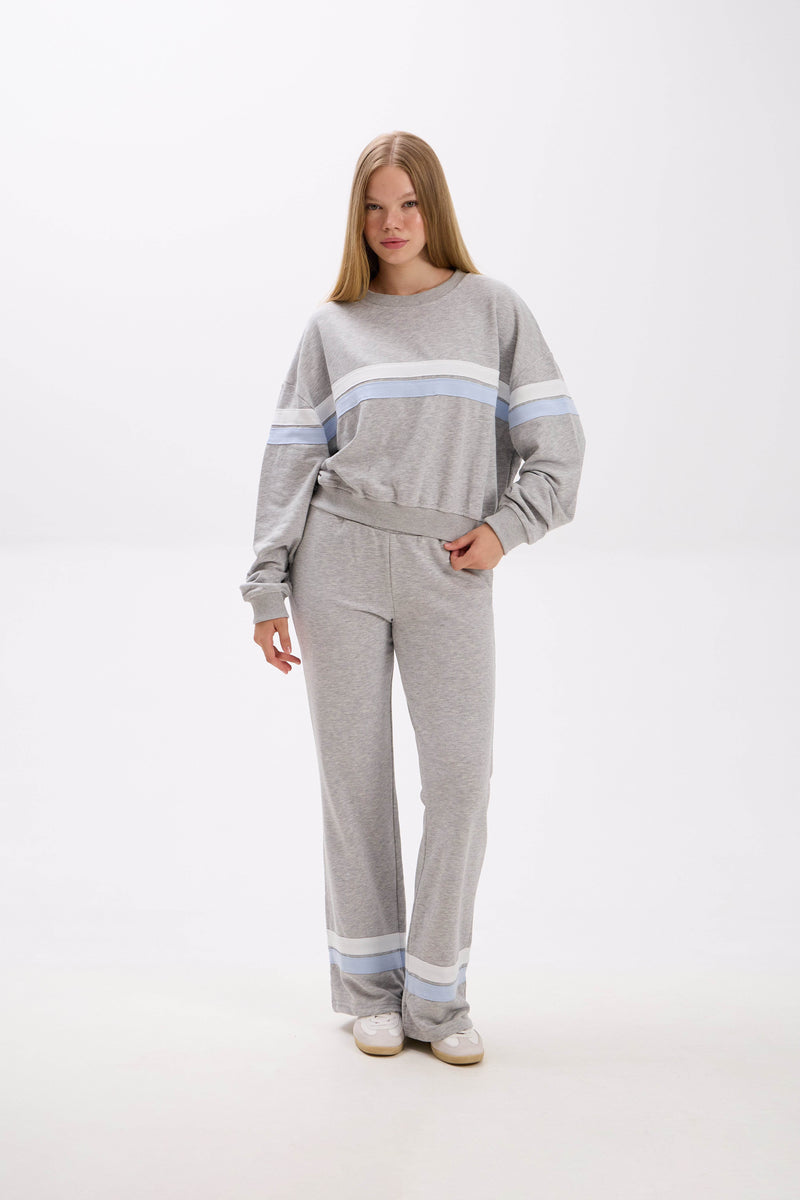Woman wearing a gray sweater and pants with blue stripes on a white background.