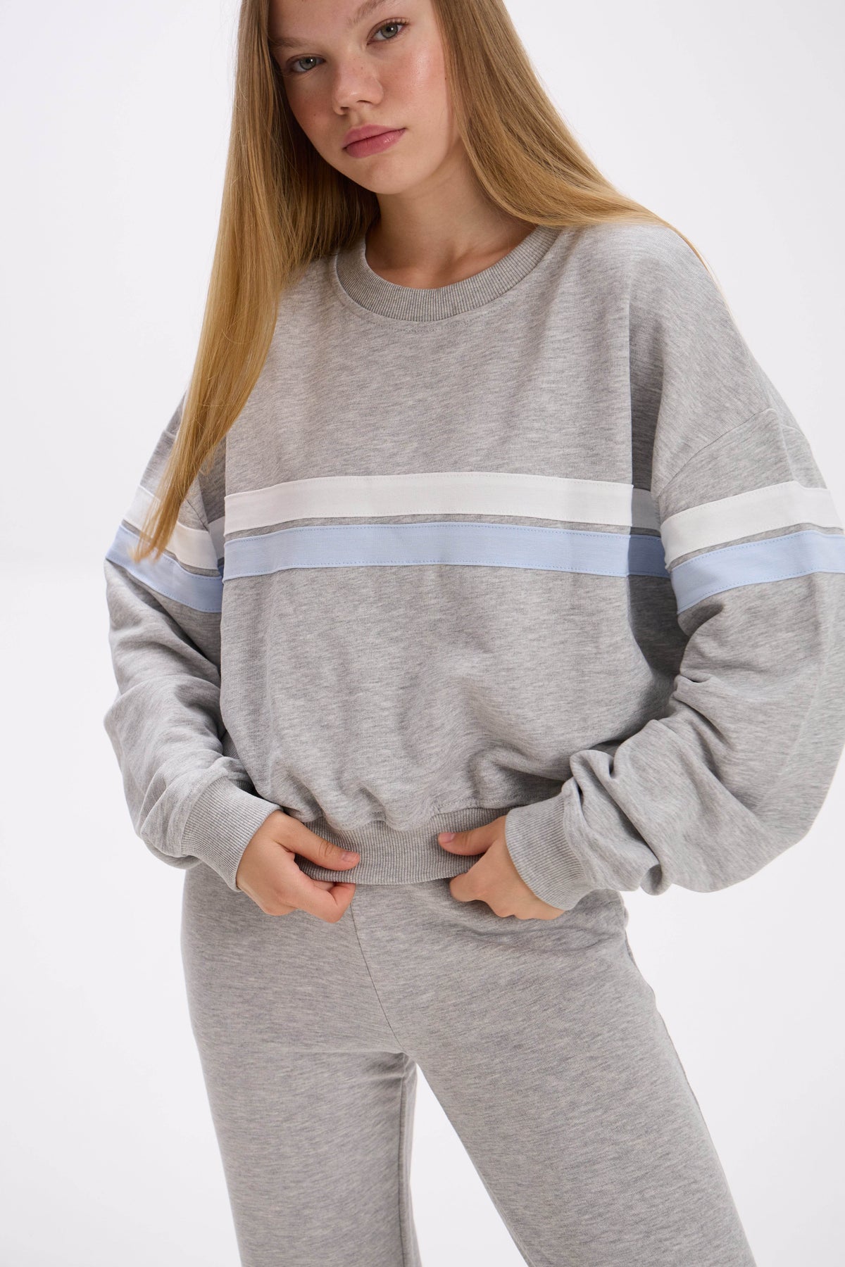 Person wearing a gray sweatshirt with a white and blue stripe on a white background.