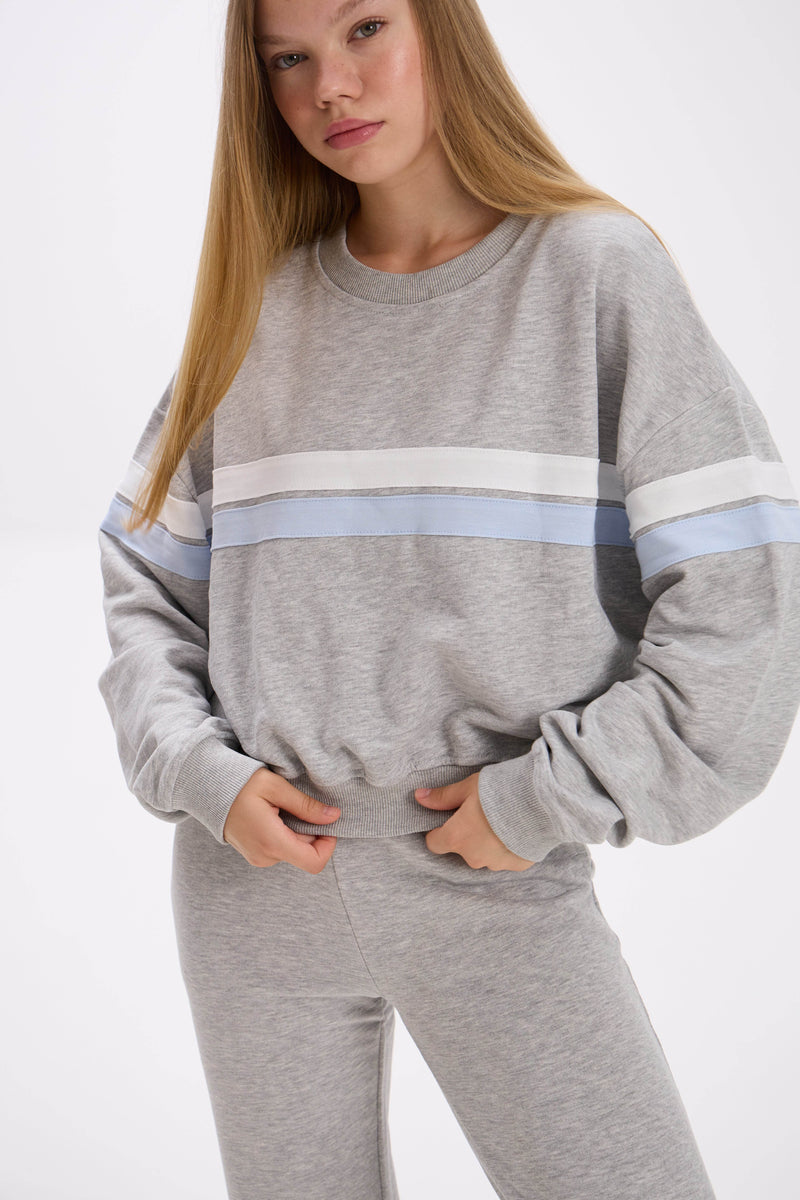 Person wearing a gray sweatshirt with a white and blue stripe on a white background.