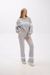 Woman wearing a gray sweater and pants with light blue stripes on a white background.