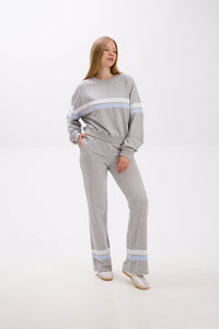 Woman wearing a gray sweater and pants with light blue stripes on a white background.