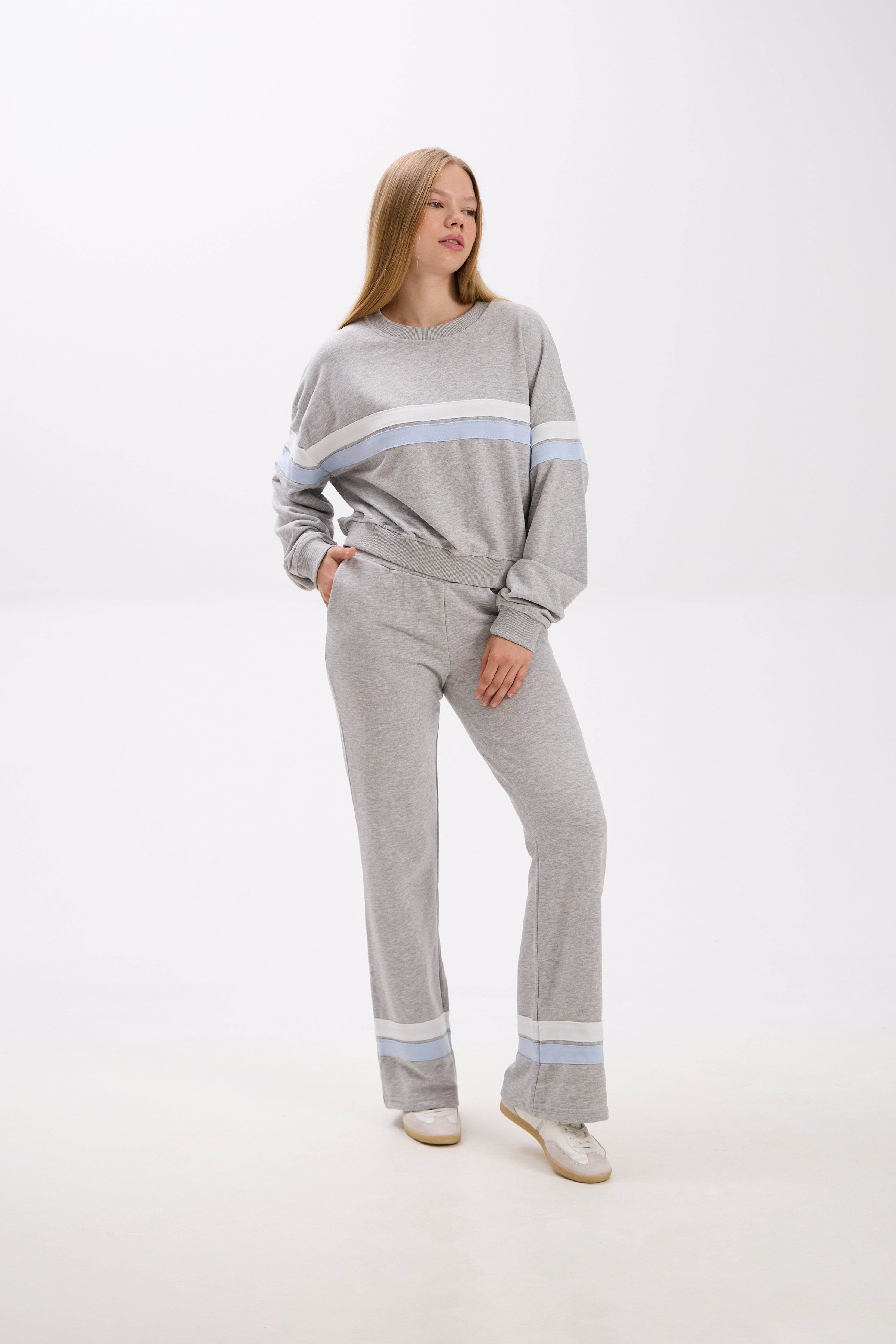 Woman wearing a gray sweater and pants with light blue stripes on a white background.