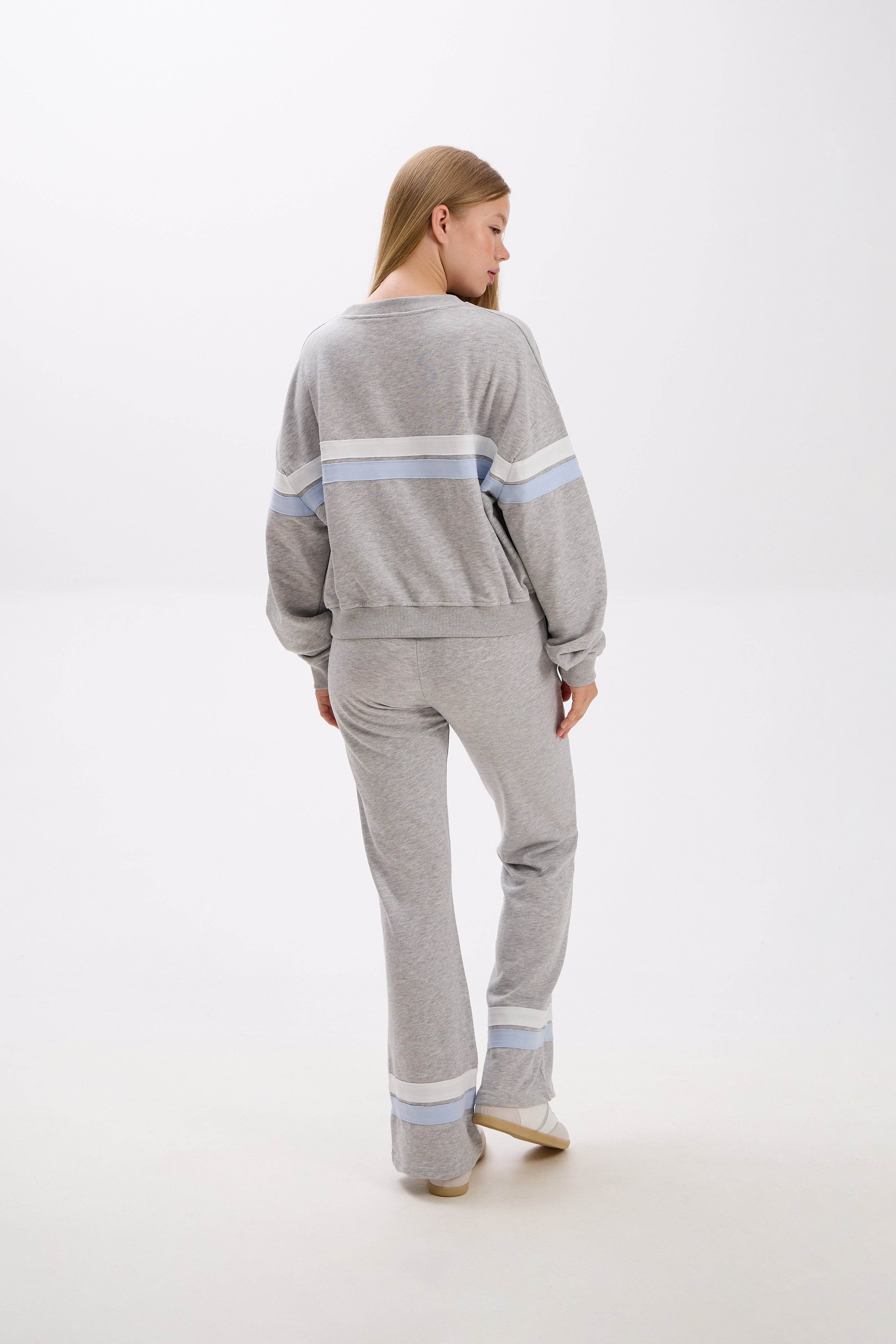 Woman wearing a gray sweater and pants with light blue stripes on a white background.