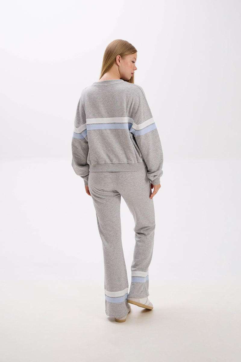 Woman wearing a gray sweater and pants with light blue stripes on a white background.