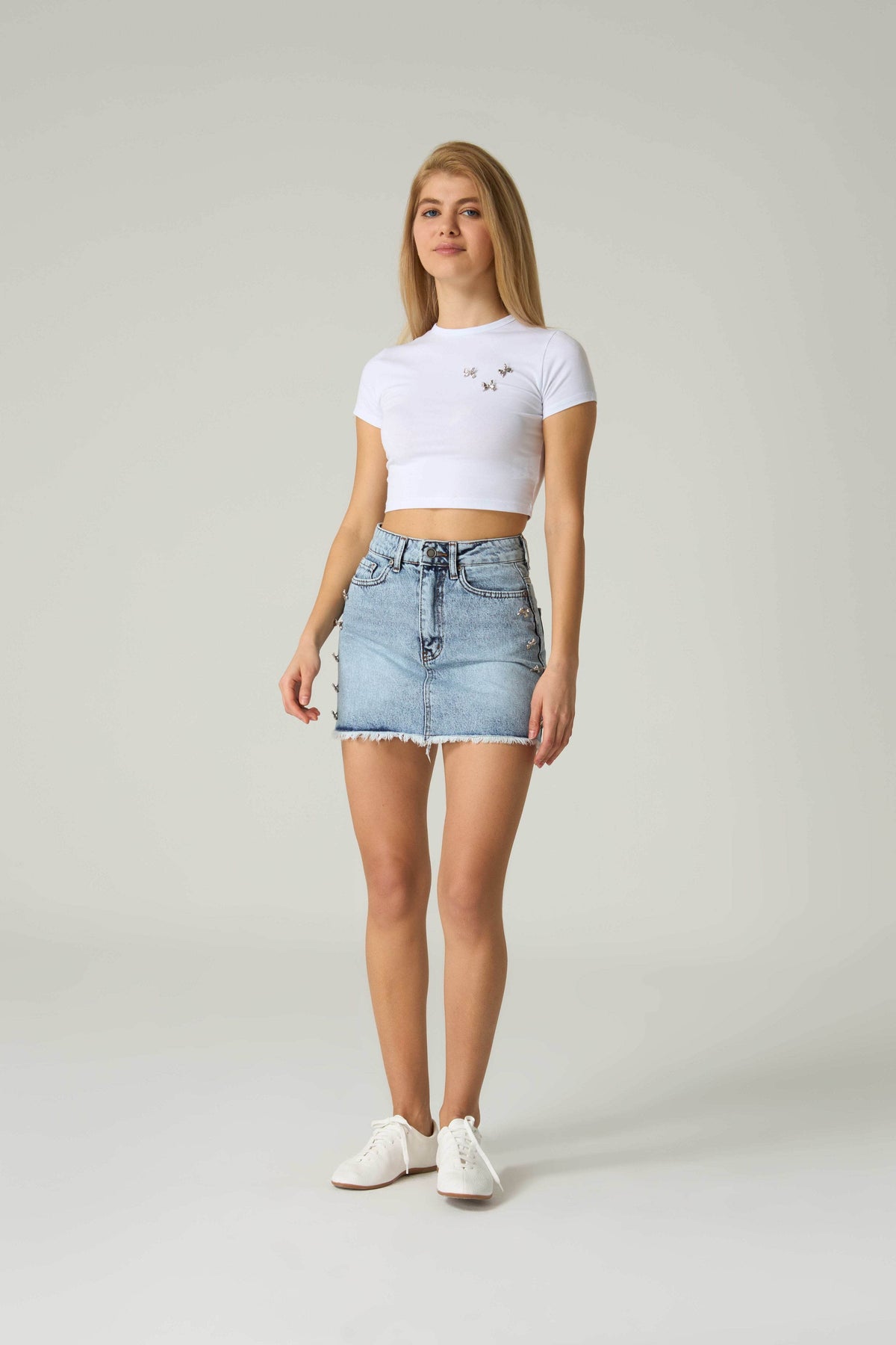 Woman wearing a white crop top and denim skirt on a plain background.