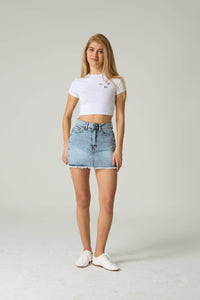 Woman wearing a white crop top and denim skirt on a plain background.