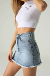 Person wearing a white crop top and denim skirt with decorative buttons on a plain background.