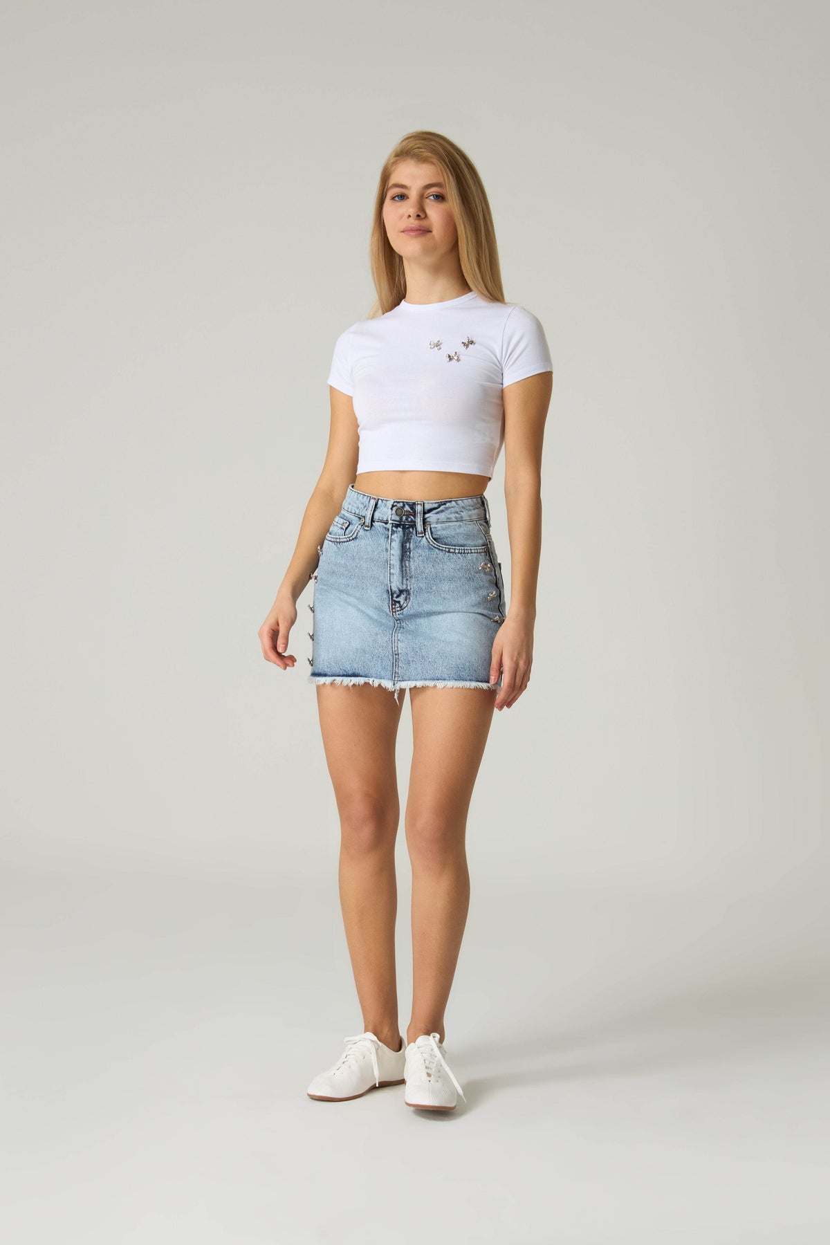 Woman wearing a white crop top and denim skirt on a plain background.